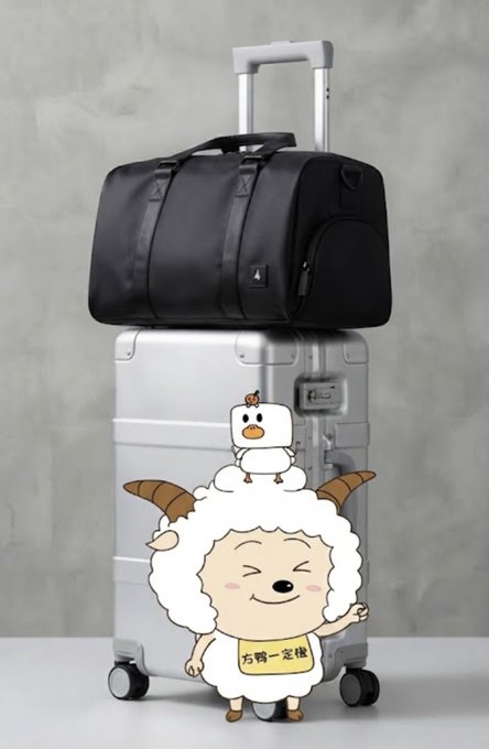 A black duffel bag sitting atop a silver hardshell suitcase, with a cartoon sheep character wearing a bib that reads '右鸭一定稳' in front.