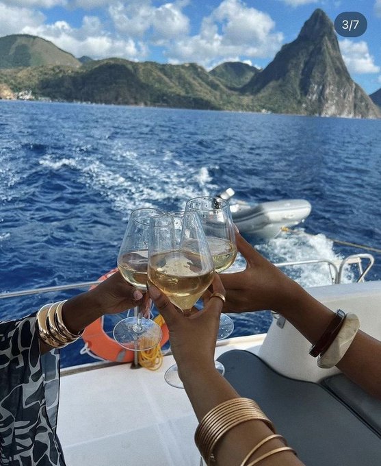 A celebratory toast with wine glasses aboard a boat, with dramatic mountain peaks rising from the ocean in the background.
