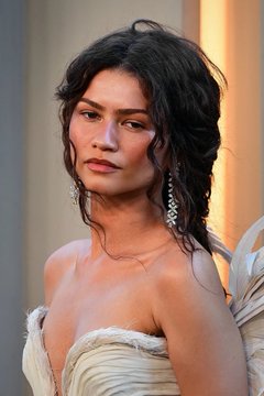 Portrait photograph of a woman with dark wavy hair wearing dangling earrings and a light-colored strapless dress.