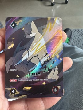A hand holding a holographic trading card featuring a Charizard-like creature with 'TURBO' text, a '4' symbol, and 'Discard an enemy Giratina with Pri...' ability description.