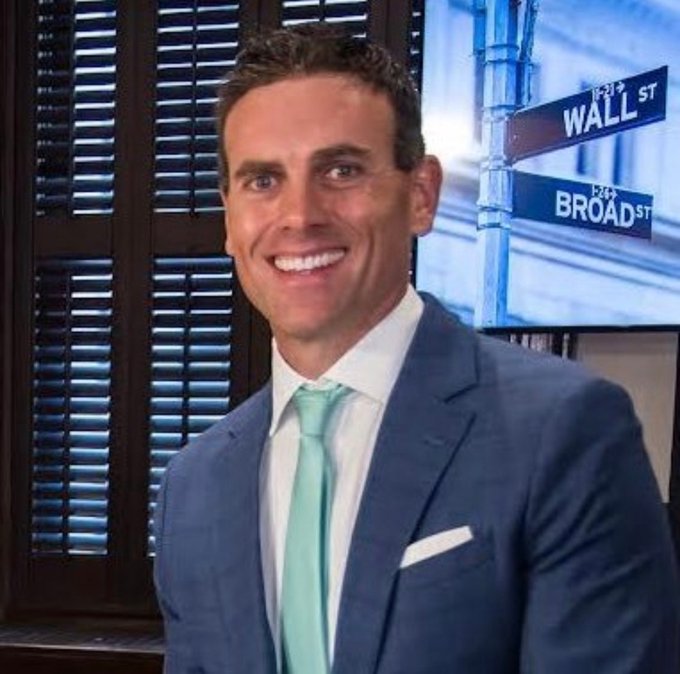 A man in a blue suit and mint green tie smiles confidently in front of a Wall Street/Broad Street street sign backdrop, reinforcing the caption's portrayal of him as a powerful Wall Street ally of Chainlink.