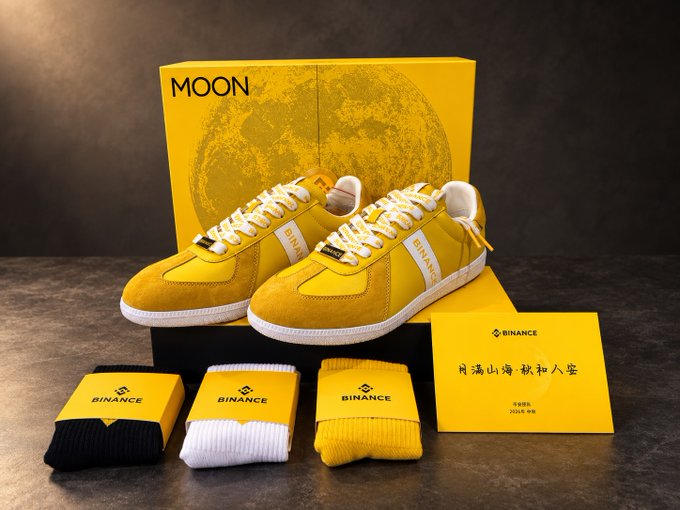 A pair of yellow Binance-branded sneakers displayed with their 'MOON' shoebox, accompanied by matching black, white, and yellow Binance socks and a card with Chinese characters.