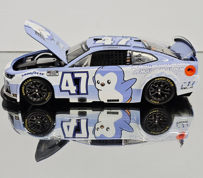 A light blue NASCAR-style race car model featuring a cartoon penguin mascot, the number 47, and sponsors including Goodyear and Pengu, sits on a reflective surface.