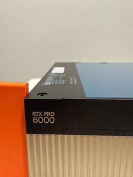 An orange object sits in the foreground, partially obscuring a piece of black and silver hardware labeled "RTX PRO 6000." The image illustrates the post's point by showing the physical, tangible GPU hardware that B3 allows users to directly own, rather than just holding a paper claim or token representing AI computing power.