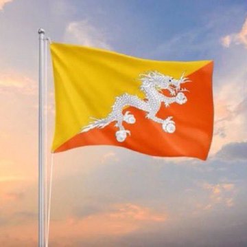 The flag of Bhutan, featuring a yellow and orange diagonal split with a white dragon, waves against a sunset sky.
