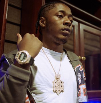 A young man with braided hair poses while showcasing his elaborate new diamond-encrusted pendant necklace and matching luxury watch, displaying his latest custom jewelry acquisitions following the sale of his previous "Clover Chain."