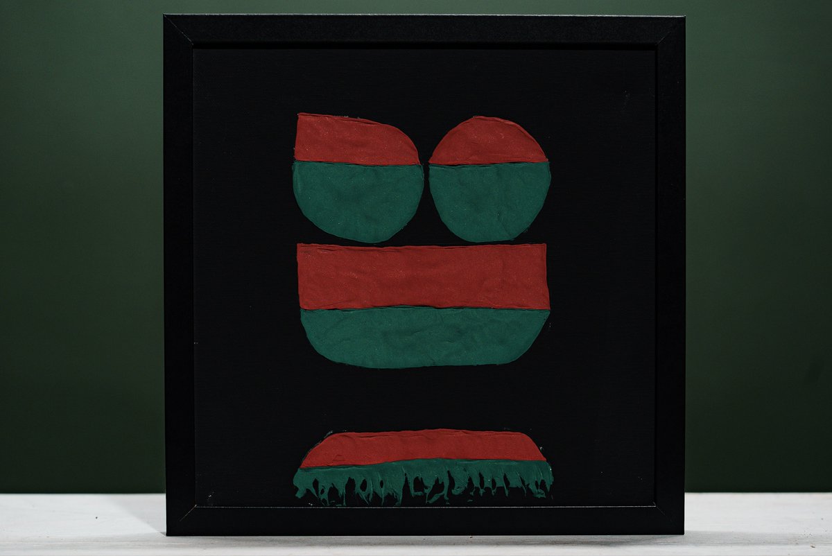 A framed piece of abstract art features red and green painted shapes on a black background, set against a dark green wall.