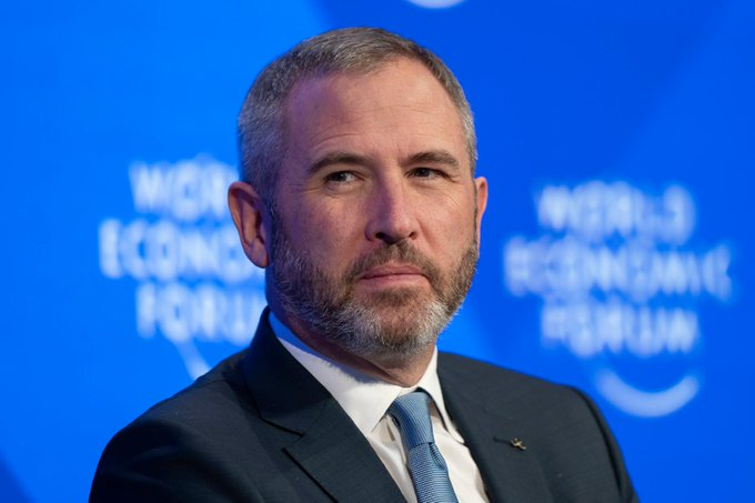 The image features a man wearing a suit and tie with a beard, standing against a blue background that reads "World Economic Forum". The man appears to be looking directly at the camera, possibly posing for a photo or giving a speech at an event related to the World Economic Forum.