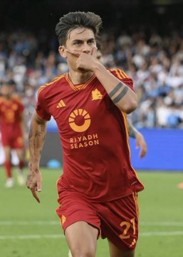 A soccer player in a red Roma jersey with 'RIYADH SEASON' sponsor logo kissing his hand in celebration on the field.