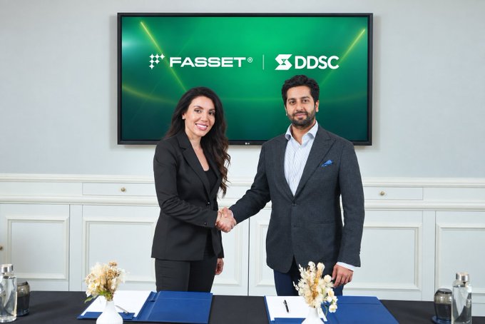 Two representatives from Fasset and DDSC shake hands after announcing their partnership to expand AED-backed digital payments across the UAE, with the companies' logos displayed on a screen behind them. This visual represents the agreement that will make Fasset the first VARA-regulated platform to list DDSC pending regulatory approval.