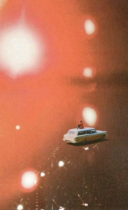 A vintage-style photograph showing a small toy car with a figure on top, floating in a hazy reddish space with bright bokeh lights.