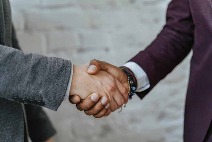 Two businessmen shake hands in front of a brick wall, symbolizing a major partnership or agreement—reflecting Citadel Securities' $400M investment in Crypto.com and the exchange's $20B valuation in its first institutional funding round.