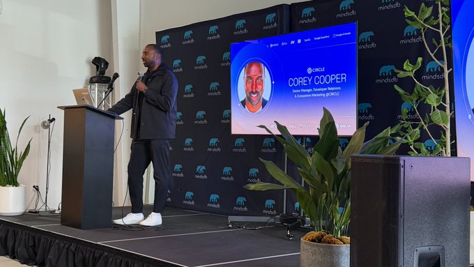 A man named 'Corey Cooper' speaks at a podium during a 'mindstudio' event, with his name and title 'Senior Manager, Developer Relations & Enablement Marketing at NVIDIA' displayed on the screen behind him.