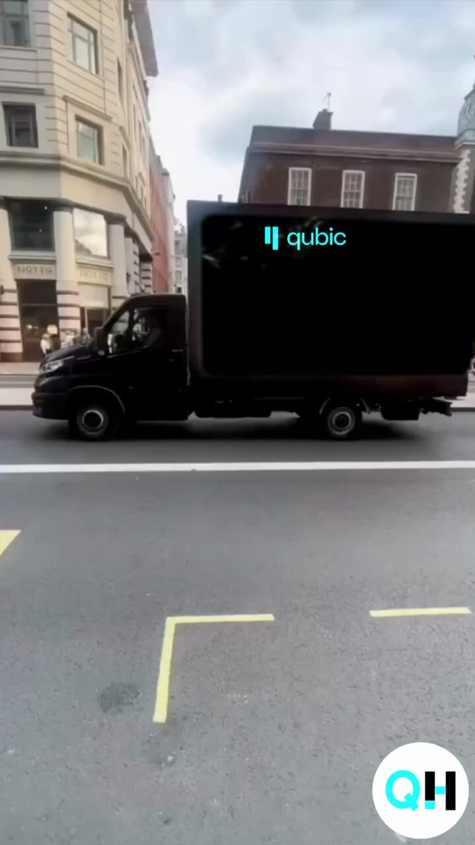 The image features a black delivery truck driving down a city street, with a yellow line painted on the road ahead of it. The truck has a "Qubic" logo displayed on its side, indicating that it's associated with the company Qubic. The text in the image reads "$Qubic ?".