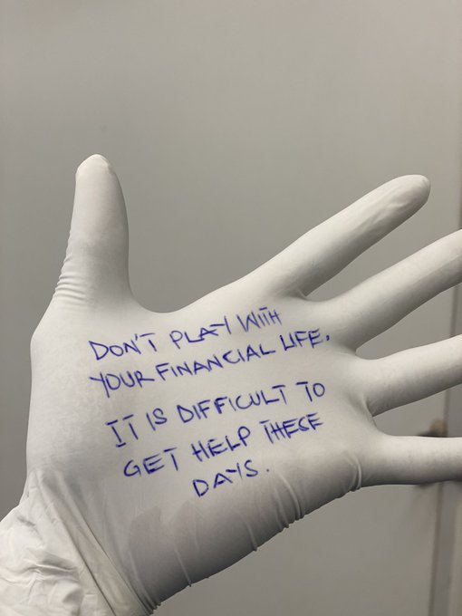 A gloved hand displays handwritten blue text reading "Don't play with your financial life, it is difficult to get help these days." The image visually reinforces the post's morning message by pairing a cautionary warning about financial stability with a clean, clinical aesthetic.