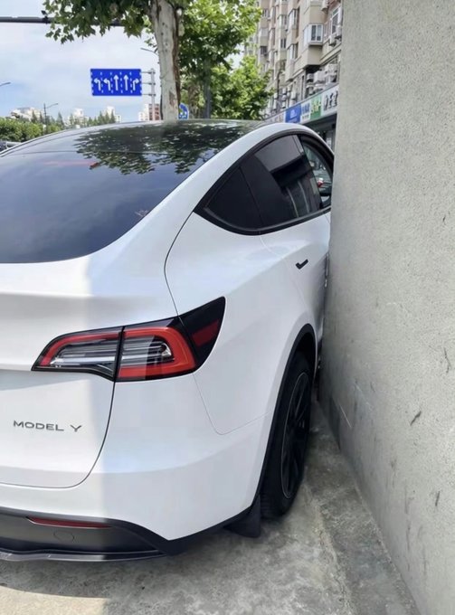 A white Tesla Model Y parked extremely close to a concrete wall in a parking spot.