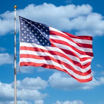 An American flag waving on a flagpole against a bright blue sky with scattered white clouds.