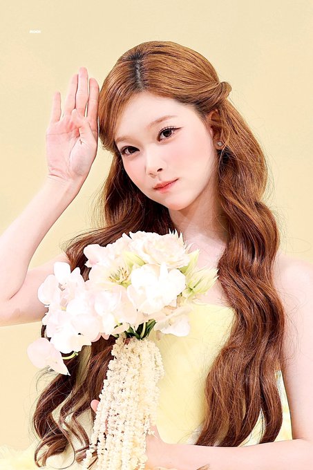 A woman with long auburn wavy hair, wearing a pale yellow dress, poses with her hand near her face while holding a bouquet of white flowers. The image features a watermark reading "Picsiix" in the top left corner, and aligns with the accompanying post referencing TSUKI (a member of the K-pop group Billlie) from a photoshoot dated 260921.