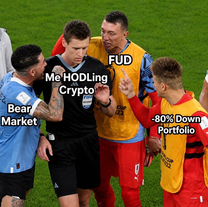 A meme showing soccer players and a referee at the 2022 World Cup, with labels added: 'Bear Market' on the blue-jersey player, 'Me HODLing Crypto' on the referee, 'FUD' on the Uruguay player, and '-80% Down Portfolio' on the Belgium player.