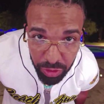A man with glasses, a beard, and a white jersey reading "Beach B..." leans into the camera in a nighttime outdoor setting. The image accompanies a post about Drake's "Stake" curse being blamed for preventing Lionel Messi from winning a second World Cup title.