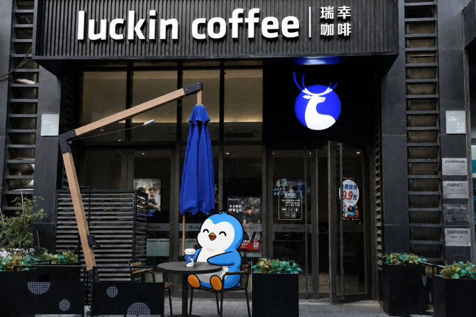 The exterior of a Luckin Coffee (瑞幸咖啡) shop featuring its blue deer logo and a cute penguin mascot sitting at an outdoor table.