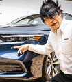 A man pointing at a dark blue Honda SUV outdoors, smiling at the camera.