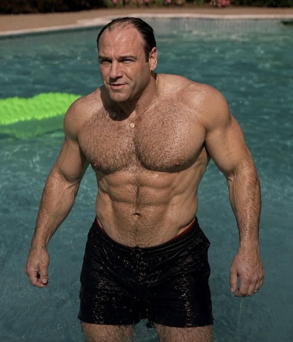 A muscular, hair-chested man wearing black swim trunks stands in a swimming pool with a green float visible behind him.