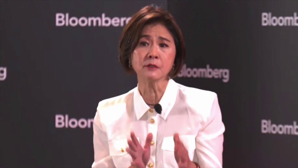 The image features a woman in an elegant white dress standing confidently against a black backdrop, likely during a presentation or speaking event. The text at the bottom of the image indicates that this could be related to UBS banking giant's statement on cryptocurrency allocation for Bitcoin and other crypto assets. The main subject is focused on her message, emphasizing her expertise and authority in the topic she discusses.