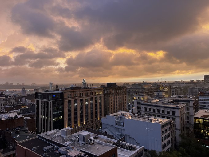 A sunset cityscape view shows buildings under dramatic orange and gray clouds.
