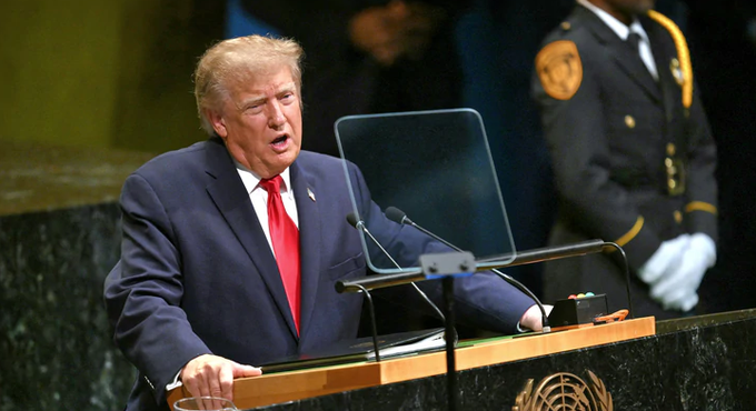 Donald Trump speaks at the United Nations General Assembly podium, with a security officer visible in the background.