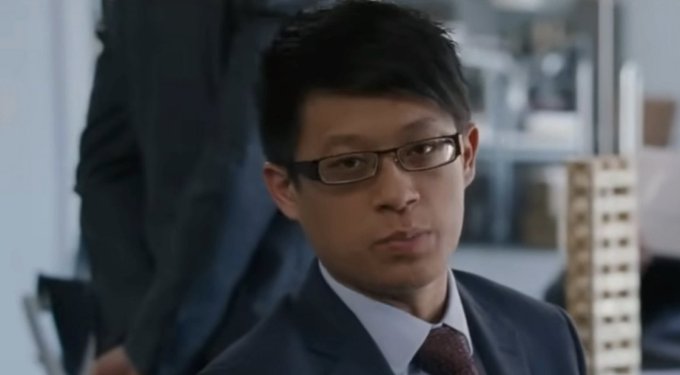 A man in glasses and a dark suit with a red tie looks sideways with a serious, skeptical expression, appearing to be in an office setting with a model building visible behind him. The image seems to convey a judging or unimpressed reaction, fitting the meme's commentary on the financial app situation.