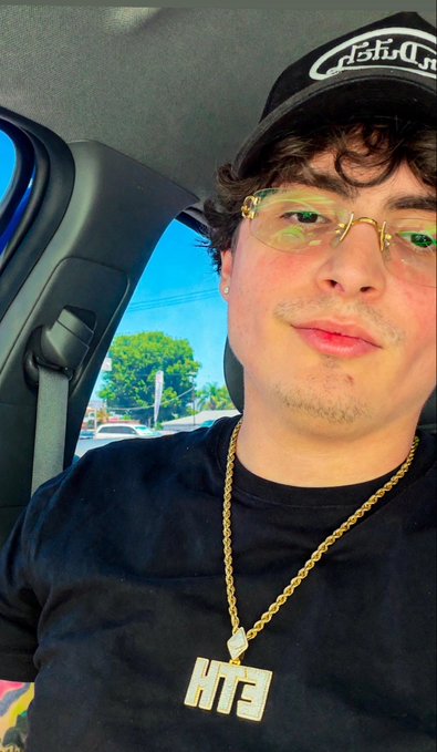 A young man wearing a black Ashbury cap and gold chain with an "HT3" pendant takes a selfie in a car, with the post noting "This is me" to present his personal style alongside his reference to an "Ape."