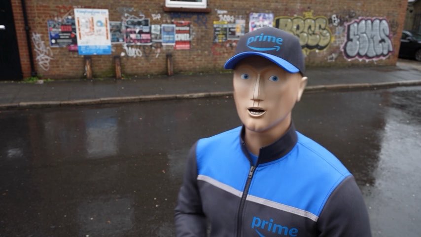 A figure wearing a Prime delivery uniform jacket and cap stands on a wet street, featuring a smooth, expressionless mask with simple painted features.