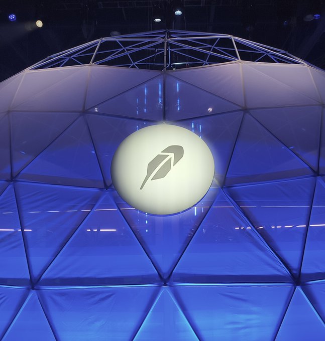 An illuminated white Robinhood feather logo centered on a large geodesic dome structure lit with purple and blue lights.