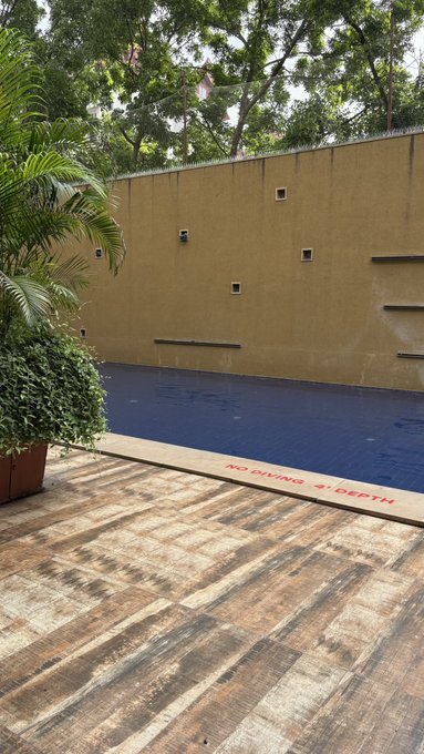 A photograph of an outdoor swimming pool area with a wooden deck, a yellow wall, and red text painted on the pool's edge that reads 'NO DIVING 9' DEPTH'.