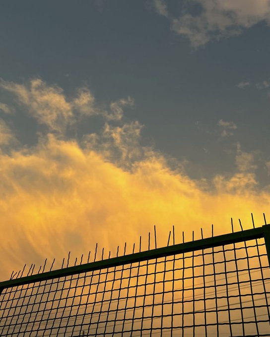A silhouette of a metal fence with spiked tops against a sunset sky filled with golden and blue clouds.