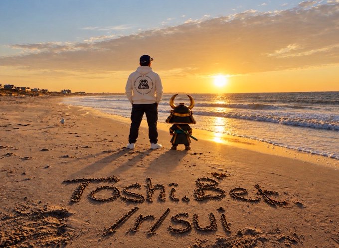 A serene beach sunset scene featuring a person in a hoodie and a samurai figure standing by the water, with 'Toshi.Bet /r/sui' written in the sand.