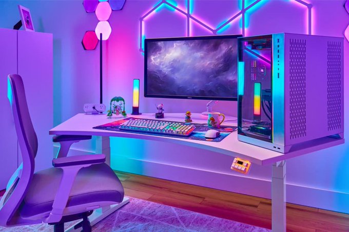 A vibrant gaming setup features a white desk with an RGB keyboard, monitor displaying a nebula wallpaper, a PC tower with a glass side panel, and a gaming chair, all illuminated by purple and pink hexagonal and triangular wall lights.