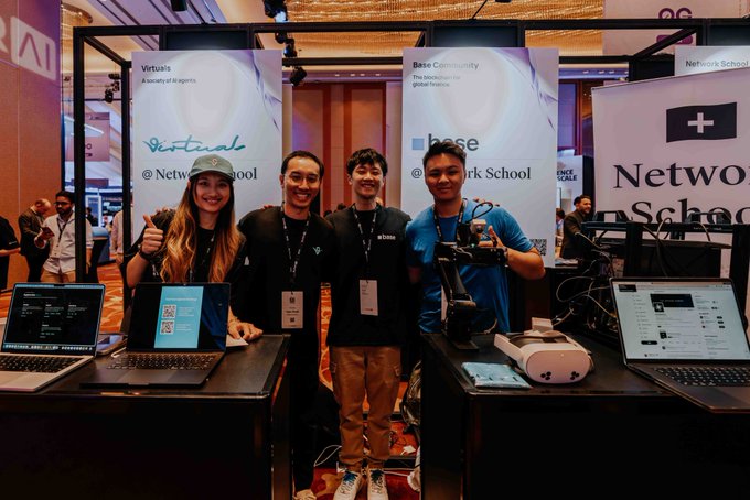 The image features a group of four people standing next to several laptops, including two open laptop computers and one closed laptop computer. They are posing for a photo at an event or convention related to technology and networking. The background includes banners that read "Base & Virtuals Family", which suggests the theme of the event is related to virtualization and networking technologies.
