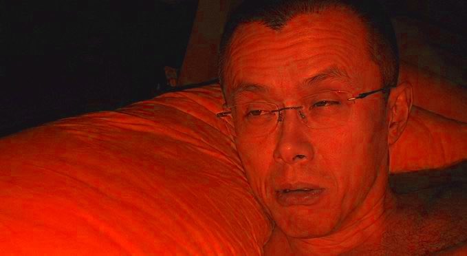 A man with rimless glasses rests his head on an orange-lit pillow, his face and surroundings bathed in a warm, reddish glow. The saturated orange tones across the image create a visual nod to 10/10, evoking the playful "orange" meme celebrated on October 10th.