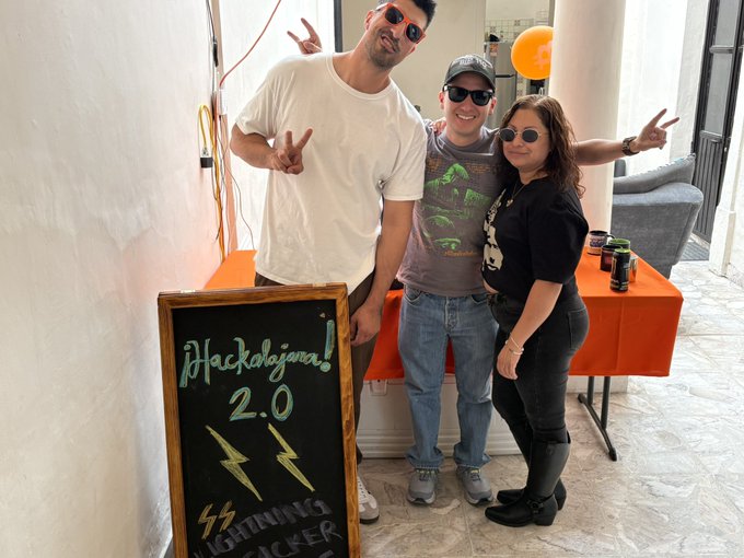 Three people posing at a 'Hackdojo! 2.0 Lightning Hacker' event, with a chalkboard sign in the foreground.