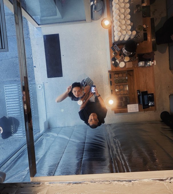 An upside-down photo taken inside a cafe shows a man and a woman posing together, with a coffee counter visible in the background.