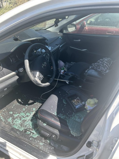 The interior of a Volkswagen car showing a broken driver's side window with shattered glass scattered across the seat and floor, indicating a break-in.