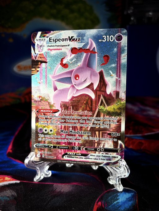 A holographic Espeon VMAX Pokémon trading card (#310) is displayed on a stand, showing its 'Solar Revelation' ability and 'Max Mindstorm' attack.