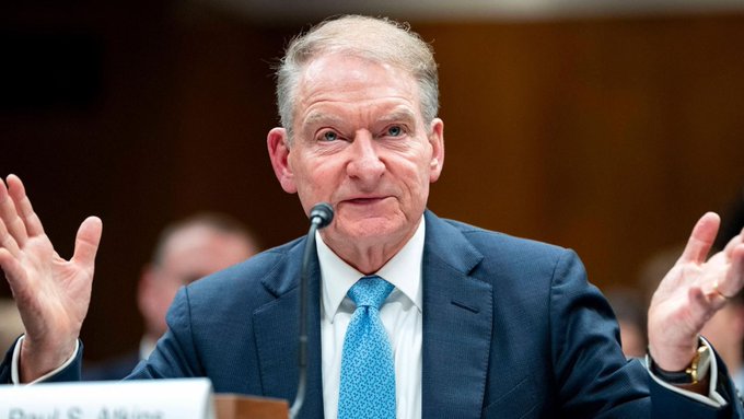 SEC Chair Paul Atkins is shown speaking at a hearing, with a partial nameplate visible reading "Paul S. Atkins," gesturing with both hands raised as he testifies on crypto regulation and his support for the CLARITY Act ahead of today's Senate vote.