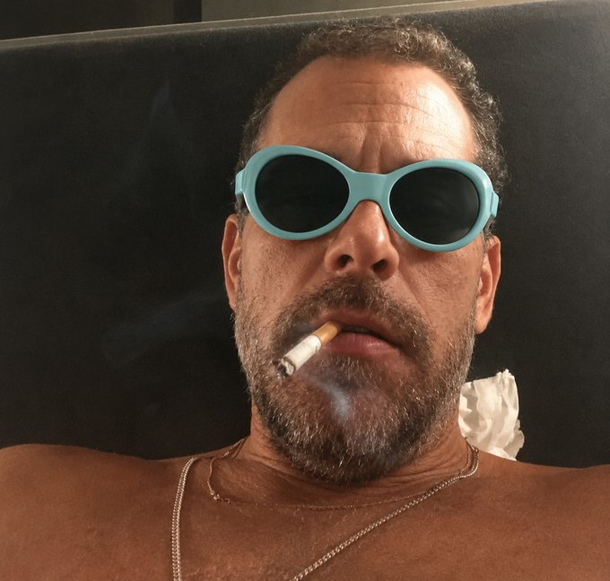 The image features a man wearing sunglasses, holding a cigarette, and smoking it while lying down. The caption of the photo includes an exclamation mark that reads "HYPE is going to three digits and there’s nothing you can do about it". This suggests that the image might be related to a humorous or lighthearted post on social media where the man's sunglasses and cigarette are being exaggerated for comedic effect, possibly to make people laugh.

The main focus of the image is the man with his sunglasses and cigarette in hand, while the caption adds an element of humor by exaggerating the details surrounding him.
