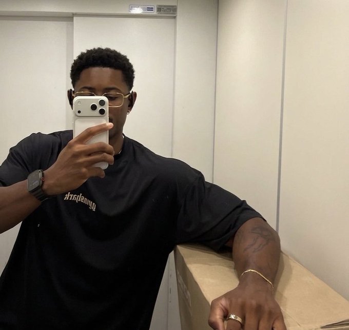 A young man wearing a black "Amiri" t-shirt takes a mirror selfie with his phone, accessorized with glasses, a watch, a bracelet, and a ring, fitting the "showing up" vibe of the post about starting another day fresh.