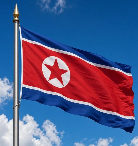 The flag of North Korea waving on a flagpole against a blue sky with scattered clouds, displaying its distinctive red star in a white circle on a red field, bordered by blue and white stripes.
