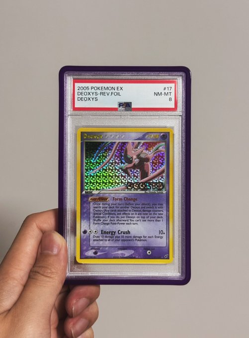A hand holding a graded PSA 8 NM-MT 2005 Pokemon EX Deoxys Reverse Foil card (#17) in a protective slab.
