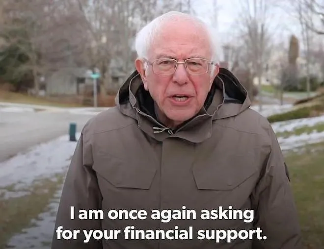 An older man with white hair and glasses stands outdoors in a winter setting wearing a brown parka, with a famous meme caption reading 'I am once again asking for your financial support.'